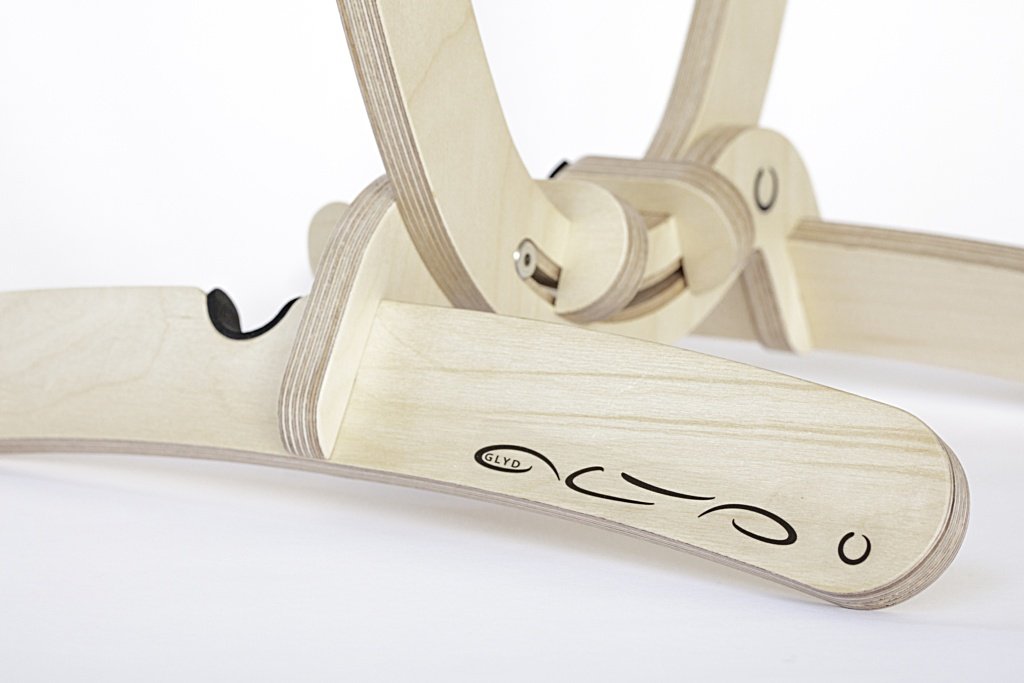 Close up cropped image showing curved wooden foot in foreground made from clear varnished birchwood with GLYD O name and Logo showing prominent on this front facing foot. In the background you can see the tail holders, other foot and bottom of the cradle,
Image is taken on a 45 degree angle. Transparent background.