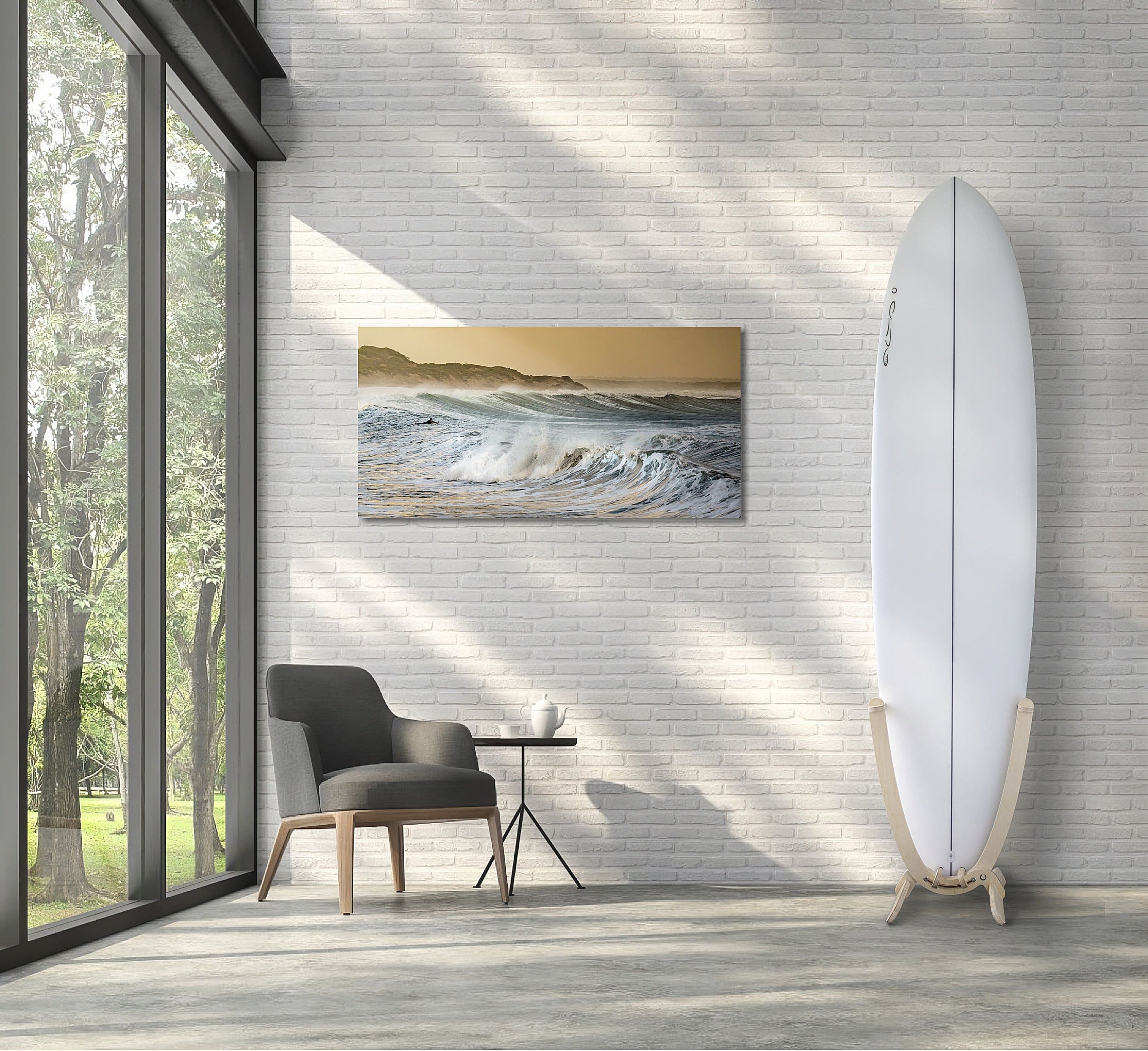 An all white Surfboard with a GLYD O decal on its nose, is mounted in a GLYD O surfboard rack. The rack with board is standing on a concrete floor to the right of the image against a white brick wall. There is a picture of waves on the wall to the left of the board and rack, a window on the left edge of the image and a chair and side table on the floor near the window. The room has much filtered light and shadows.
The surfboard rack and surfboard really pop in this picture and the image gives you an idea of the feeling and vibe the GLYD O surfboard rack brings to a room.
The Surfboard Rack is a Beautiful birchwood curved single surfboard rack in the shape of the tail of a surfboard, with hooks to hold the rails and tail and two slightly curved feet connected perpendicular to the upright curved arms. Image is taken from the front in relations to the vertical surfboard rack.